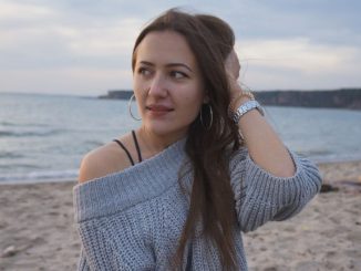 Portrait of a woman in a gray knitted sweater by the seaside, enjoying a serene moment.