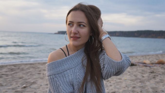 Portrait of a woman in a gray knitted sweater by the seaside, enjoying a serene moment.