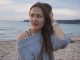 Portrait of a woman in a gray knitted sweater by the seaside, enjoying a serene moment.
